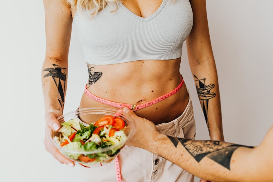 Fit woman measuring waist while holding a healthy salad bowl